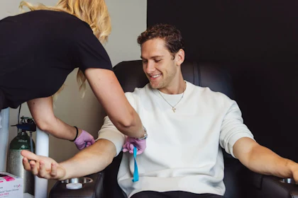 A phlebotomist drawing blood from a seated patient in a treatment chair.